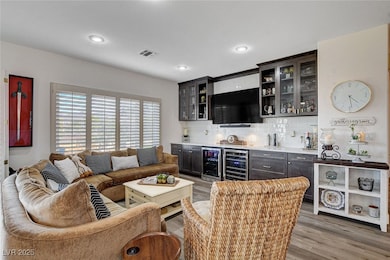 Indoor bar featuring light wood-type flooring, backsplash, glass insert cabinets, beverage cooler, and recessed lighting