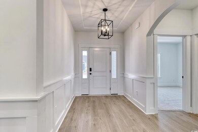 Entrance foyer with a decorative wall, light wood-style floors, arched walkways, a chandelier, and wainscoting