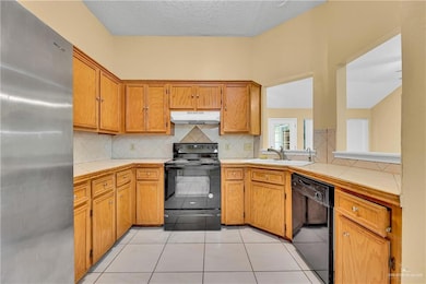 Kitchen with black appliances, backsplash, light tile patterned floors, brown cabinetry, and a textured ceiling
