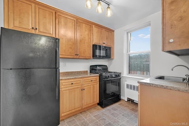 Kitchen with black appliances, radiator heating unit, brown cabinets, and hanging light fixtures