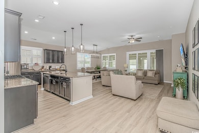 Kitchen featuring a sink, open floor plan, ceiling fan, light wood-style floors, and light stone counters
