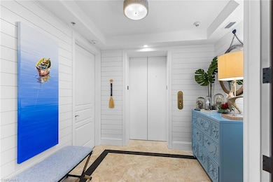 Entryway with inlaid floor details, a raised ceiling, elevator, wood walls, and recessed lighting