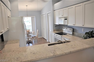Kitchen featuring white appliances, light stone countertops, white cabinetry, and light wood-style floors