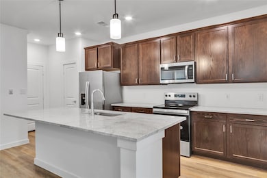 Kitchen with light wood-type flooring, a kitchen island with sink, appliances with stainless steel finishes, and a sink