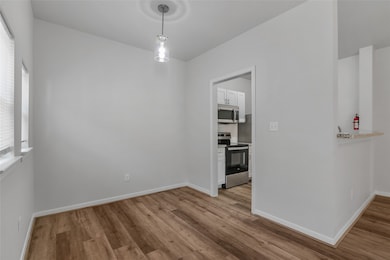 This cozy dining area features an open layout with direct access to the kitchen, perfect for easy meal prep and entertaining. The space is bright and inviting, with large windows allowing for plenty of natural light. The wood-look flooring adds warmth to the neutral-toned walls, creating a versatile space that can easily accommodate different dining setups. A modern light fixture adds a touch of style, making this dining nook both functional and aesthetically pleasing.