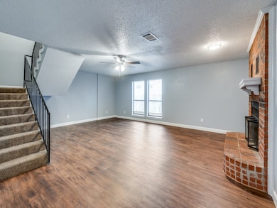 Unfurnished living room with stairway, a textured ceiling, dark wood-style floors, ceiling fan, and a fireplace