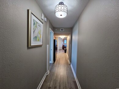 Hallway with dark wood-style floors, a textured wall, and a textured ceiling