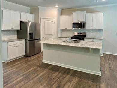 Kitchen featuring tasteful backsplash, white cabinetry, light stone counters, crown molding, and recessed lighting