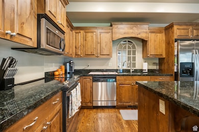 Kitchen featuring appliances with stainless steel finishes, wood finished floors, brown cabinetry, and dark stone counters