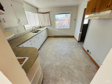 Kitchen featuring under cabinet range hood, a baseboard heating unit, and white cabinetry