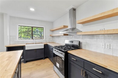 Kitchen featuring wooden counters, stainless steel range with gas stovetop, exhaust hood, open shelves, and light wood finished floors