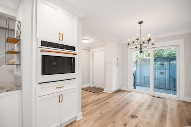 Kitchen with ornamental molding, oven, white cabinetry, light wood-style flooring, and pendant lighting
