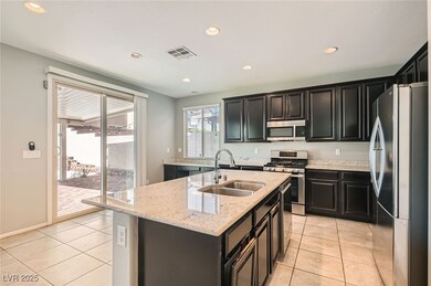 Kitchen featuring appliances with stainless steel finishes, dark cabinets, recessed lighting, a center island with sink, and light tile patterned floors