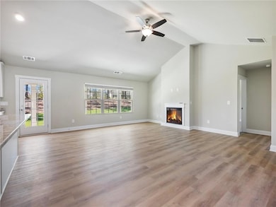 Unfurnished living room featuring vaulted ceiling, healthy amount of natural light, a glass covered fireplace, a ceiling fan, and baseboards