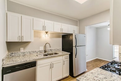 Kitchen featuring stainless steel appliances, white cabinets, light wood-style flooring, and light stone counters