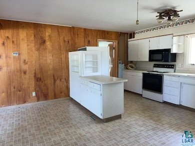 Kitchen with black microwave, white electric range oven, wooden walls, light countertops, and a peninsula