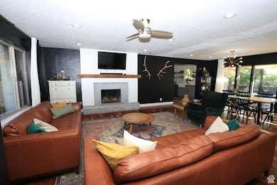 Living area with ceiling fan, wood finished floors, a brick fireplace, a textured ceiling, and a chandelier
