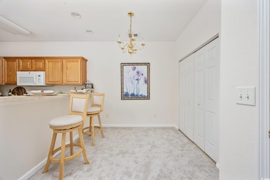 Kitchen featuring white microwave, light colored carpet, a chandelier, a breakfast bar area, and hanging light fixtures
