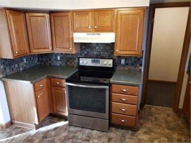 Kitchen featuring stainless steel electric range, brown cabinetry, decorative backsplash, and dark countertops