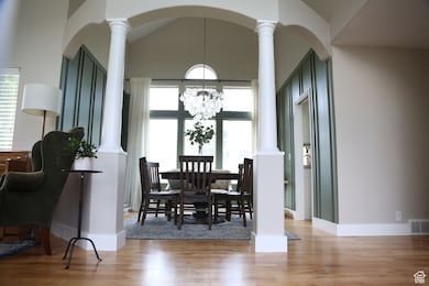 Dining area featuring ornate columns, light wood-style flooring, arched walkways, vaulted ceiling, and a chandelier