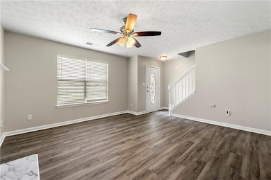 Unfurnished living room featuring a textured ceiling, stairway, dark wood-style floors, and a ceiling fan