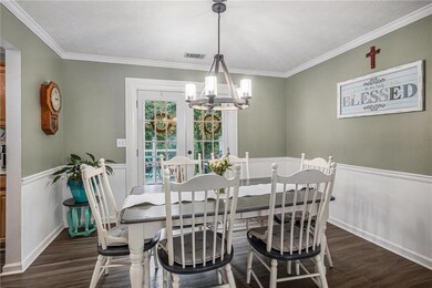 Dining space with a chandelier, dark wood-style flooring, ornamental molding, a wainscoted wall, and a textured ceiling
