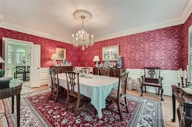 Dining room featuring wallpapered walls, ornamental molding, a chandelier, wainscoting, and light wood finished floors