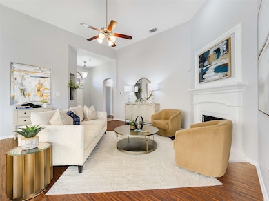 Living area with arched walkways, a fireplace, wood finished floors, and a ceiling fan