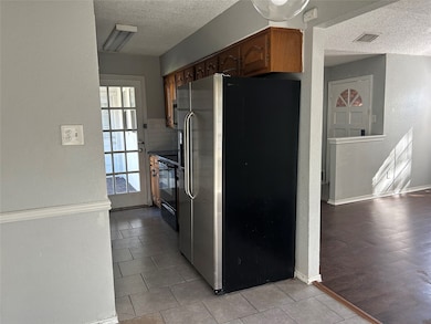 Kitchen with a textured wall, stainless steel fridge, a textured ceiling, light tile patterned flooring, and black / electric stove