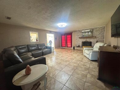 Living area featuring a textured ceiling, a brick fireplace, and light tile patterned floors