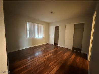 Unfurnished bedroom with dark wood-style floors and multiple closets