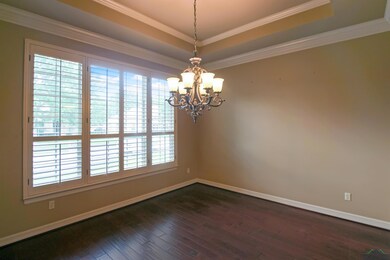 Empty room featuring a raised ceiling, a chandelier, dark wood-type flooring, baseboards, and crown molding