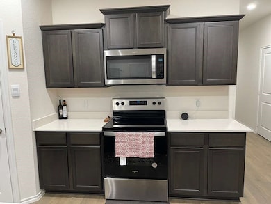 Kitchen featuring stainless steel appliances, light wood finished floors, a textured wall, and dark brown cabinetry