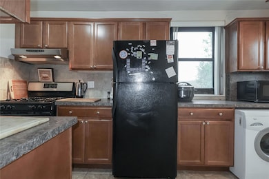 Kitchen with black appliances, washer / clothes dryer, under cabinet range hood, dark countertops, and tasteful backsplash