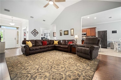Living room with wood-type flooring, a ceiling fan, ornamental molding, high vaulted ceiling, and baseboards