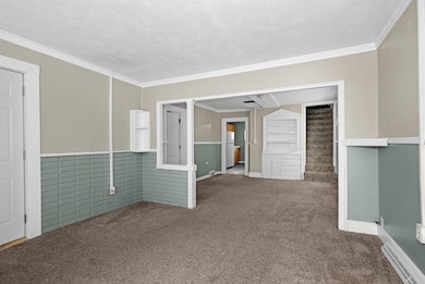 Carpeted empty room with a baseboard radiator, ornamental molding, and a wainscoted wall
