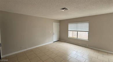 Tiled empty room with a textured ceiling and baseboards