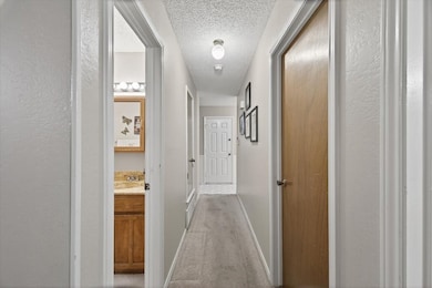 Hall featuring light carpet, a textured ceiling, and a textured wall