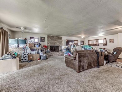 Living room featuring a stone fireplace, a textured ceiling, carpet, and a ceiling fan