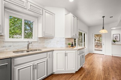 Kitchen featuring pendant lighting, white cabinets, light stone countertops, backsplash, and light wood finished floors