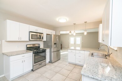 Perfect for entertaining, the family room and kitchen are divided by a seated bar with granite countertops, a timeless subway tile backsplash, all new white shaker style cabinetry, stylish lighting, and durable ceramic tile flooring.