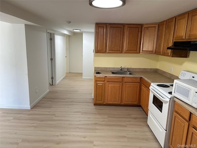 Kitchen featuring brown cabinets, light wood-style floors, under cabinet range hood, and white appliances