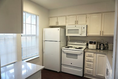 Kitchen featuring white appliances, white cabinets, light countertops, and dark wood-type flooring