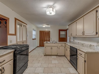 Kitchen featuring black appliances, a peninsula, cream cabinetry, and light tile patterned floors