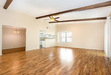 Unfurnished living room with a chandelier, beam ceiling, light wood finished floors, a ceiling fan, and high vaulted ceiling