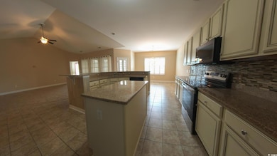 Kitchen featuring stainless steel range with electric stovetop, black microwave, a kitchen island, light tile patterned flooring, and baseboards