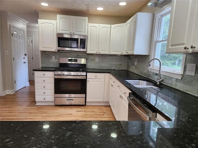 Kitchen with stainless steel appliances, dark stone countertops, white cabinets, ornamental molding, and recessed lighting