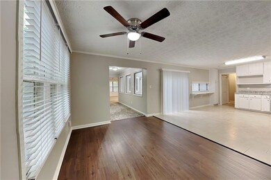 Unfurnished living room featuring a ceiling fan, a textured ceiling, light wood-style floors, ornamental molding, and baseboards