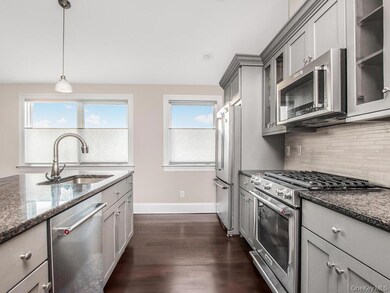 Kitchen with stainless steel appliances, pendant lighting, dark stone counters, and gray cabinetry