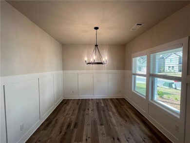 Unfurnished dining area with a chandelier, dark wood-style flooring, a wainscoted wall, and a decorative wall